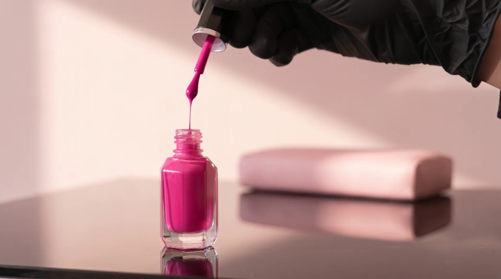 The cap of the bottle lifted by a gloved hand: a thin ribbon of fuchsia polish runs from the brush back into the faceted glass
