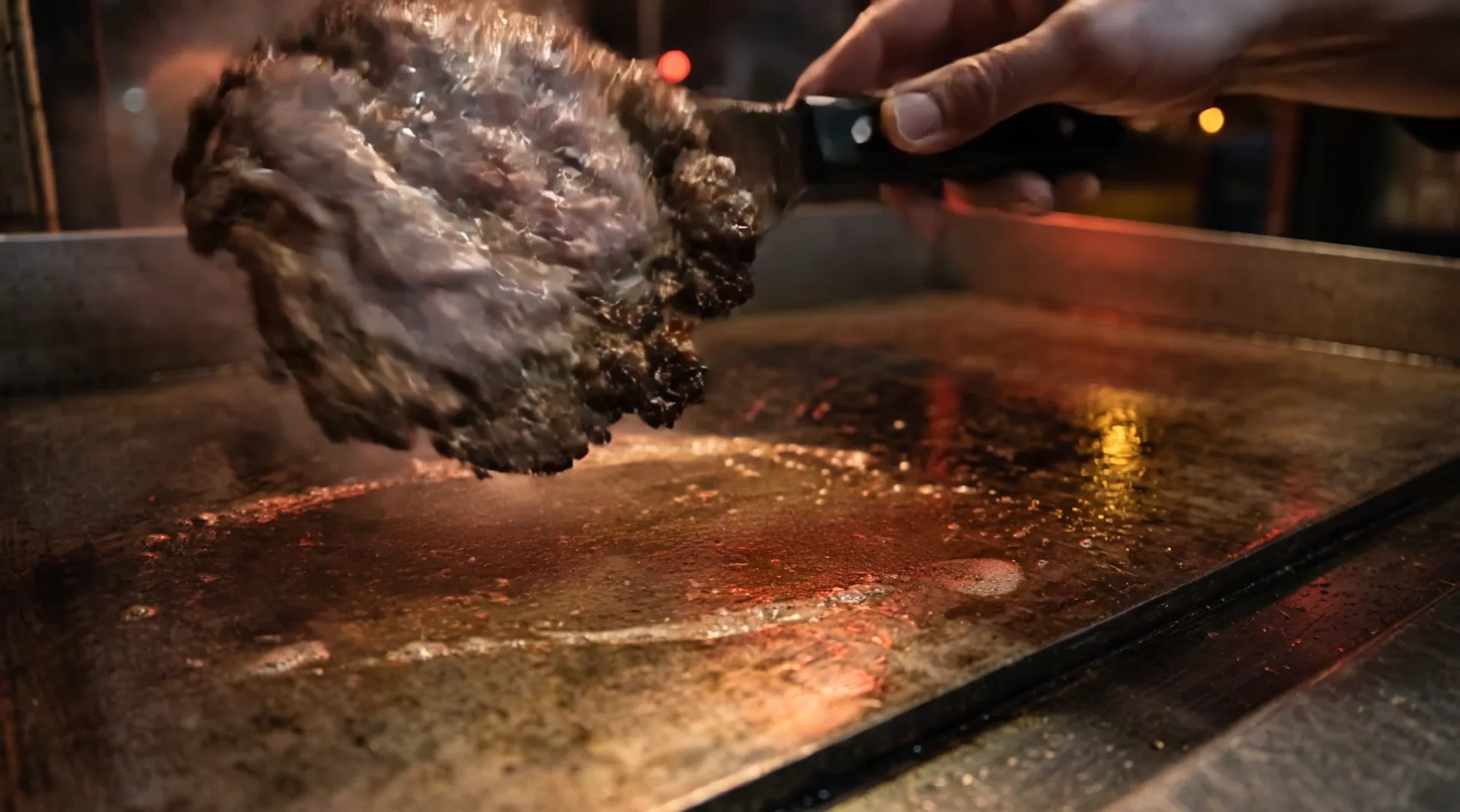 A spatula turns the thin patty over in the air above the griddle