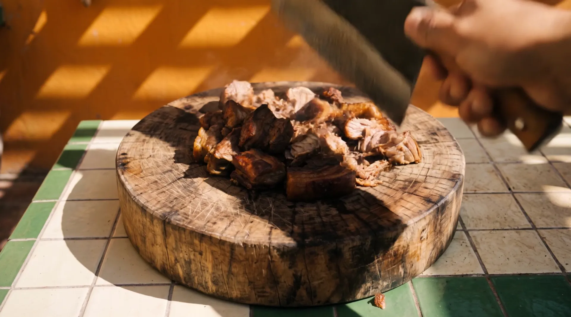 A hand with a steel cleaver chops crisp slow-cooked pork on a round wooden block