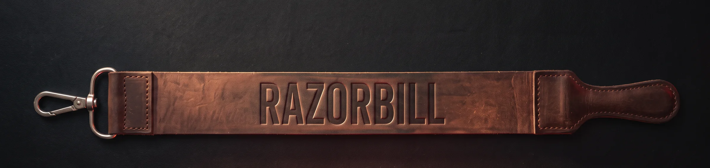 A leather razor strop laid out flat on black, the name Razorbill stamped into the leather