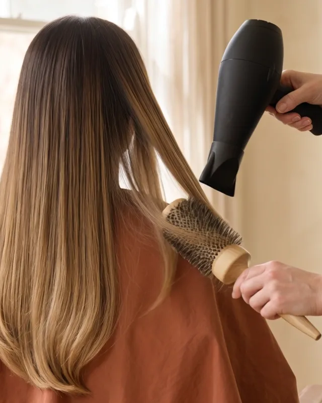A round brush and a dryer draw a section of honey-gold hair down